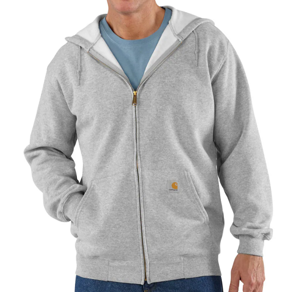 A person wears a Carhartt TS0122 LooseFit MediumWeight Full-Zip Sweatshirt in Carbon Heather over a blue t-shirt and jeans. The hoodie features a small Carhartt logo by the pocket, white hood lining, and a loose-fit style.