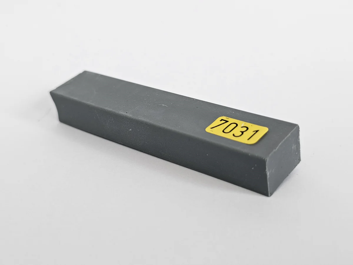 A rectangular, dark gray metal bar with a beveled edge lies on a white surface—commonly used for repair tasks.