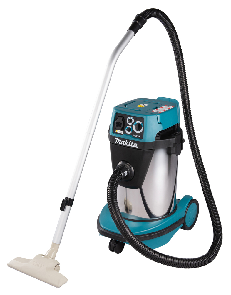 A Makita VC3211H Dust Extractor with blue and silver canister, black hose, silver tube, beige floor attachment, upright on castors.