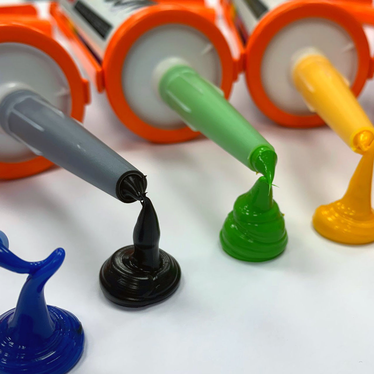 A tube of silicone sealant with rainbow-colored stripes, a white background, and a separate pointed nozzle cap beside it.