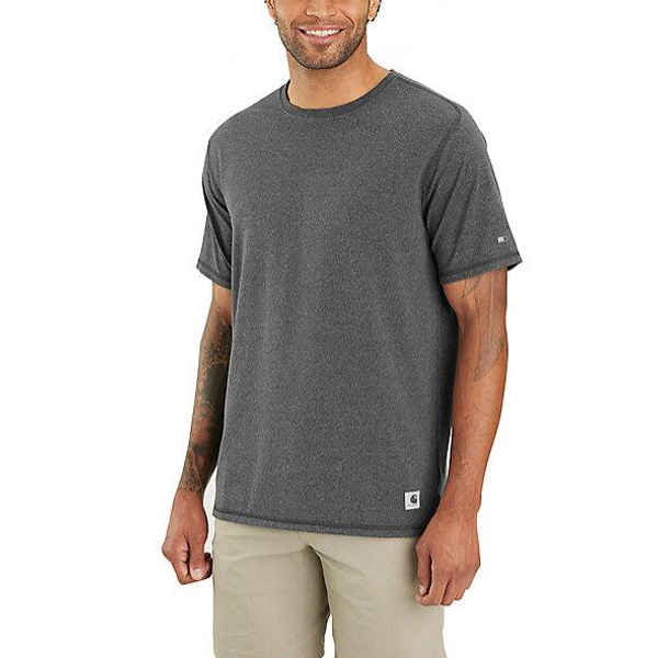 A smiling person stands to the side, displaying tattooed arms in a gray Carhartt T-shirt and light beige shorts.