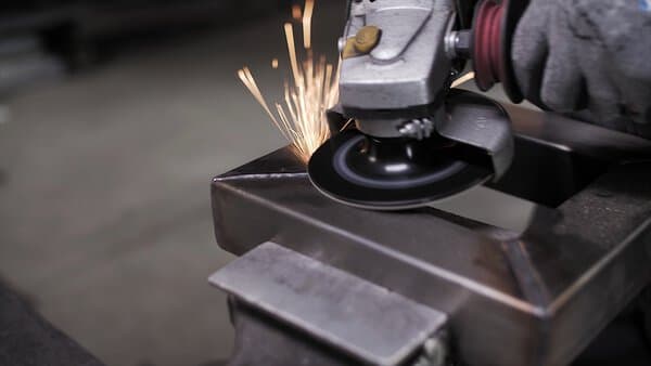 A close-up of a person using an angle grinder with 60 grit fibre discs on metal, creating sparks whilst wearing protective gloves.