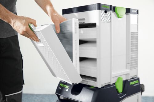A person handles a large rectangular filter for a Festool air purifier or dust extractor, mainly white with green and black accents.