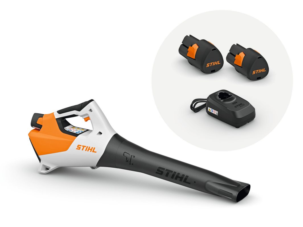 A Stihl cordless leaf blower in orange, white, and black with a close-up inset of two rechargeable batteries and a charging base.
