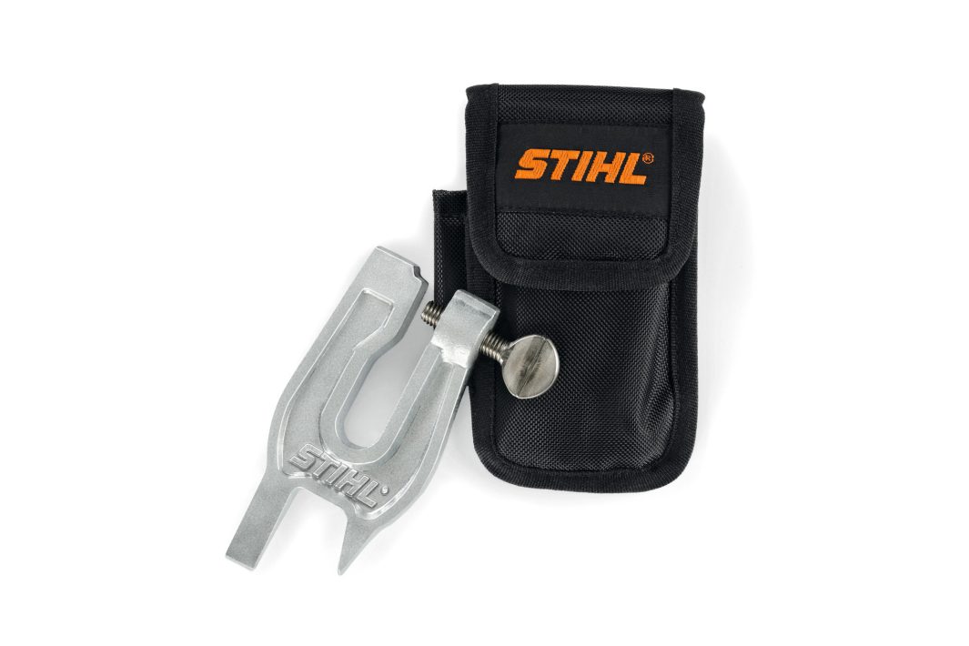 A metal STIHL filing guide tool with a screw knob is beside a black carrying pouch with the orange STIHL logo on a white background.