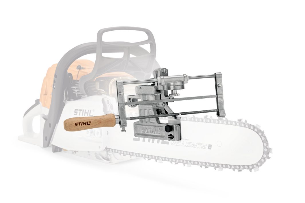 A close-up of a STIHL chainsaw with a metal sharpening guide with a wooden handle, the rest of the chainsaw faded in the background.