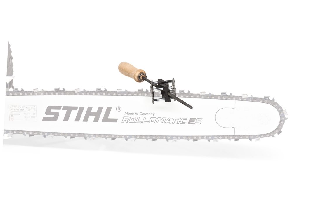 A STIHL Rollomatic ES chainsaw bar with a sharpening tool attached to the chain, featuring a wooden handle and metal guide.