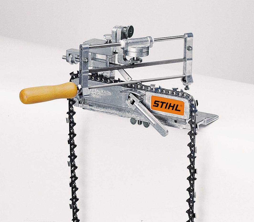 A STIHL chainsaw sharpening tool with a wooden handle is mounted on a chainsaw chain, featuring a metal frame on a plain background.