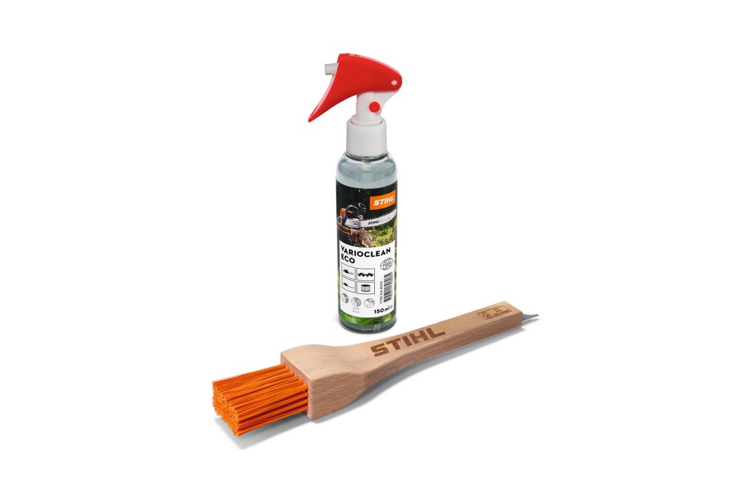 A bottle of STIHL cleaning spray with a red nozzle beside a wooden-handled brush with orange bristles on a white background.