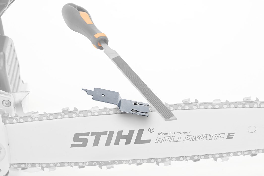 A flat file and combination tool are placed on the guide bar and chain of a STIHL Rollomatic E chainsaw for maintenance.