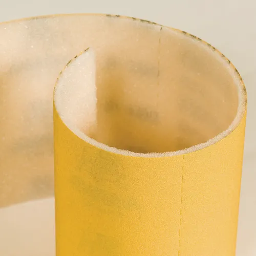 A close-up of the Mirka Goldflex Soft 115 x 125 mm Perforated Roll, partially unrolled, displays its rough textured abrasive surface and white backing, making it ideal for detailed sanding tasks.