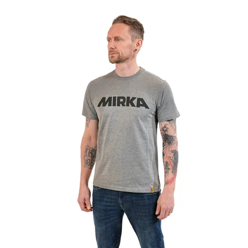A man with tattoos on his arms wears a signature grey T-shirt and blue jeans, standing against a plain white background.