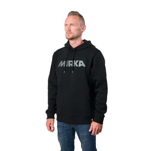 A man with short hair, dressed in a black hoodie, stands against a white background and wears blue jeans.