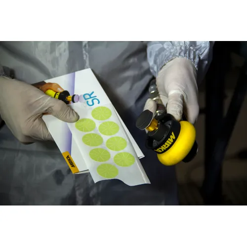 A gloved individual holds a tool and a sheet of Mirka Polestar 32mm PSA Sanding Discs (100pc), preparing for a sanding or polishing task.