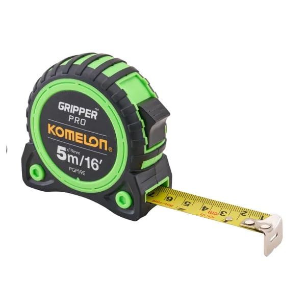 A green and black Komelon Gripper Pro tape measure is extended, displaying its yellow measuring tape. The tape shows measurements up to 5 metres or 16 feet.