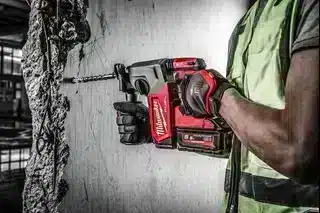 A person wearing a high-visibility vest uses a Milwaukee M18FPP6L3-503B 18v 6pc Fuel Power Pack - 3 x 5.0ah Batteries cordless rotary hammer drill to bore into a concrete pillar.
